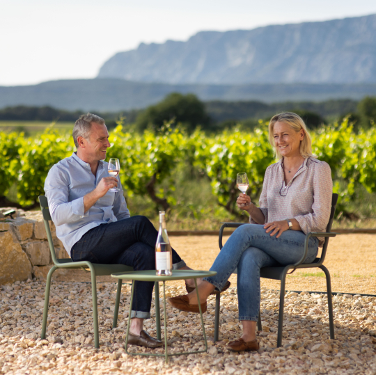 Un couple trinque au vin dans un vignoble pittoresque avec des montagnes en arrière-plan.