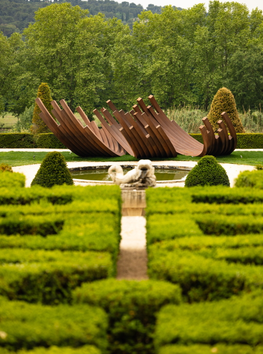 Sculpture moderne dans un jardin à la française, avec un bassin et des haies parfaitement taillées.