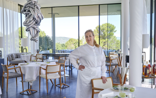 Une cheffe souriante dans un restaurant élégant avec vue sur la nature.