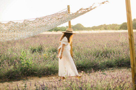 Une femme en robe blanche se promène dans un champ de lavande au coucher du soleil.