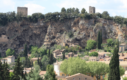 Vue panoramique d'un village perché sur une falaise calcariée, avec des tours médiévales.