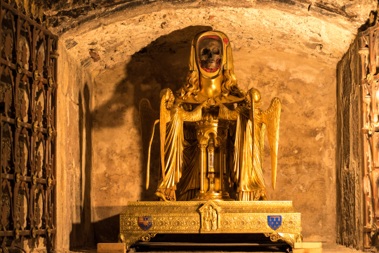 Statue dorée de Saint-Denis, tenant un crâne, dans une chapelle médiévale sombre.