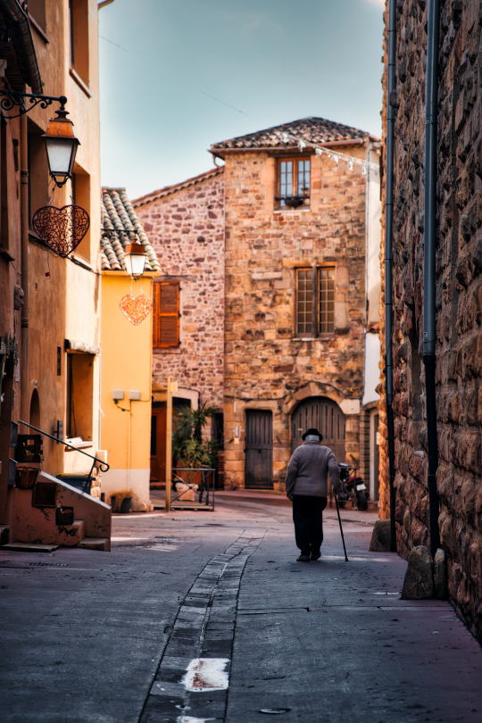 Un vieil homme se promène dans une ruelle pavée d'un village pittoresque au coucher du soleil.