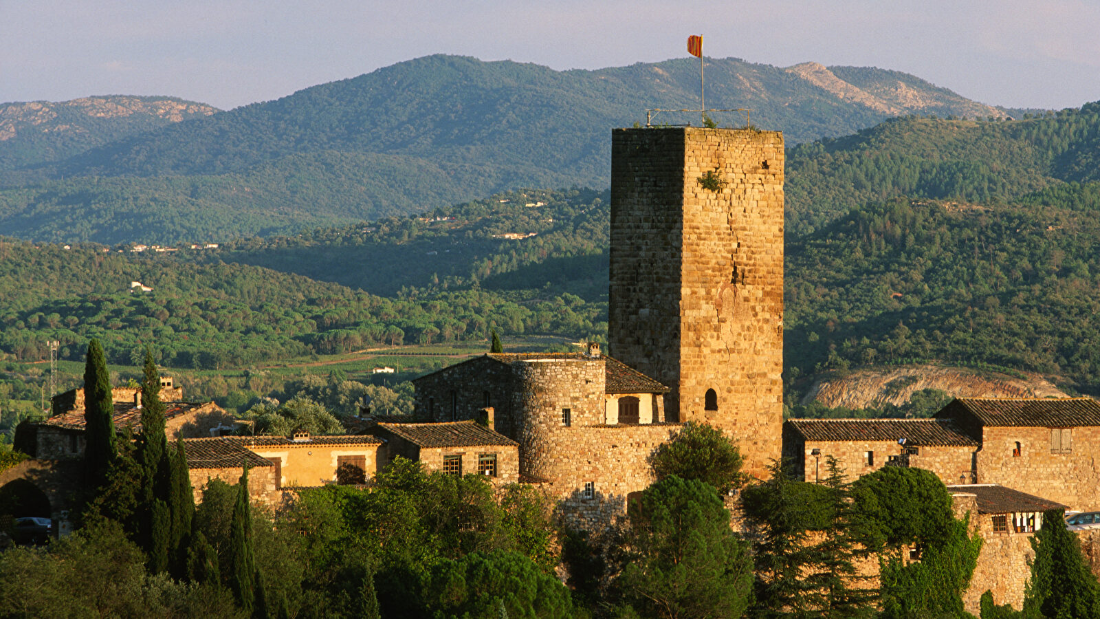 Une tour médiévale imposante se dresse dans un paysage rural et montagneux.