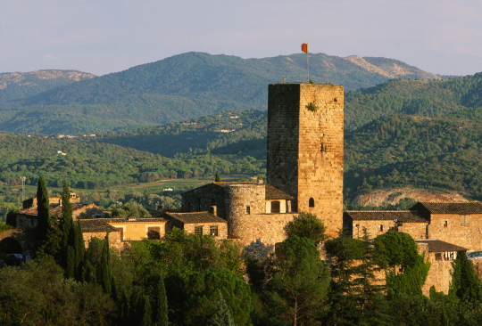 Une tour médiévale imposante se dresse dans un paysage rural et montagneux.