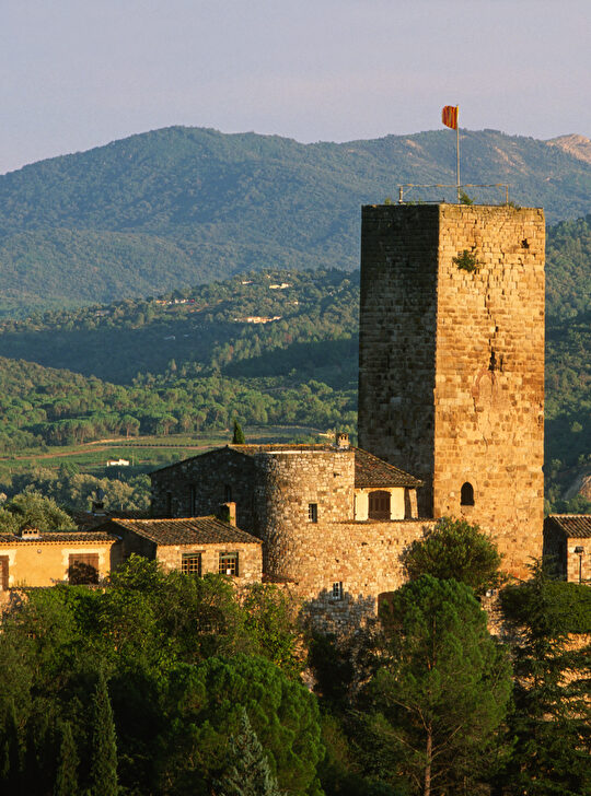 Une tour médiévale imposante se dresse dans un paysage rural et montagneux.