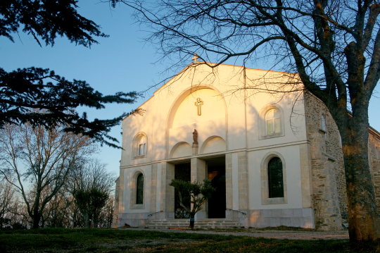 Une église en pierre illuminée par le soleil couchant, entourée d'arbres dénudés.