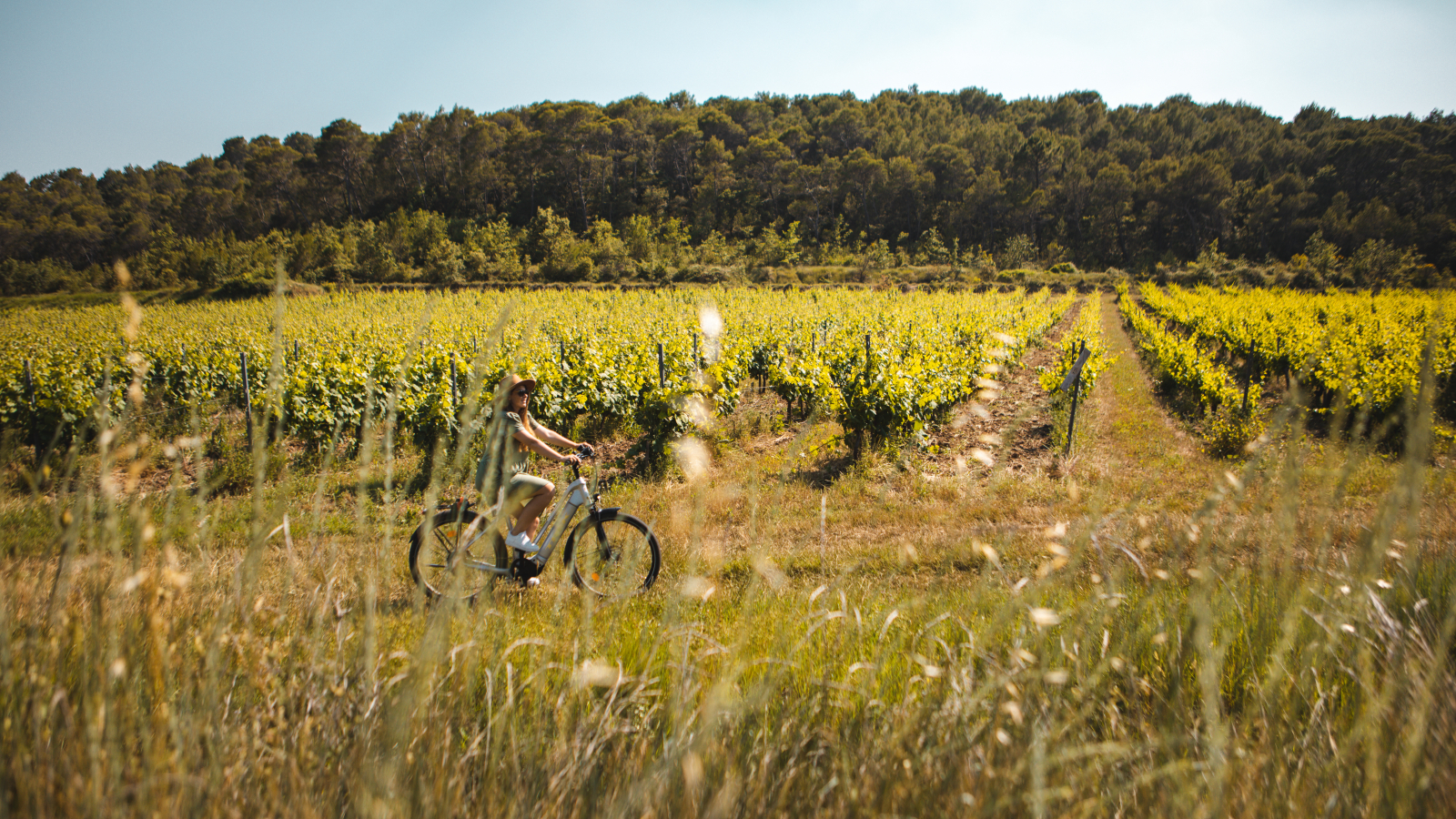 Une femme pédale sur un vélo électrique dans un champ de tournesols ensoleillé.