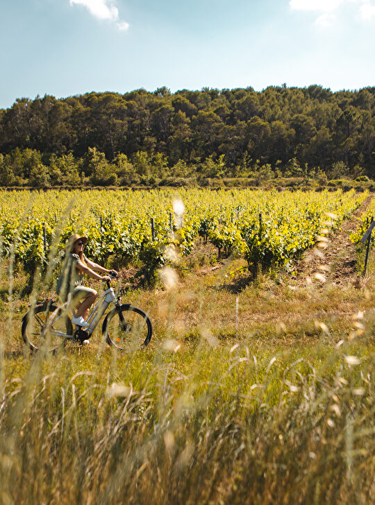 Une femme pédale sur un vélo électrique dans un champ de tournesols ensoleillé.