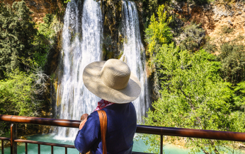 Une femme admire une cascade impressionnante dans un cadre naturel verdoyant.