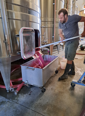 Un homme manipule du jus de raisin dans une cuve de fermentation industrielle.