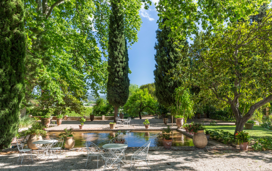 Un magnifique jardin provençal avec un bassin, des cyprès et des bancs en fer forgé.