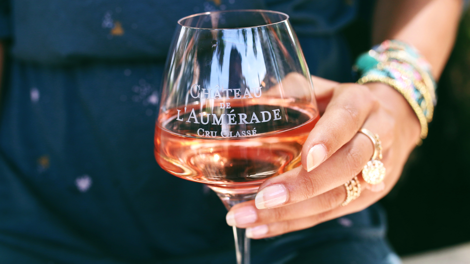 Un verre de vin rosé du Château l'Aumérade, délicatement tenu par une main.