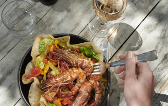 Une main mange un plat de fruits de mer frais avec du vin sur une table en bois.