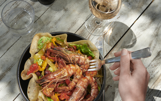 Une main mange un plat de fruits de mer frais avec du vin sur une table en bois.