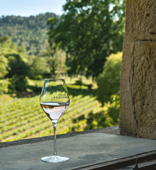 Un verre de vin rosé de Provence devant un paysage vallonné et verdoyant.