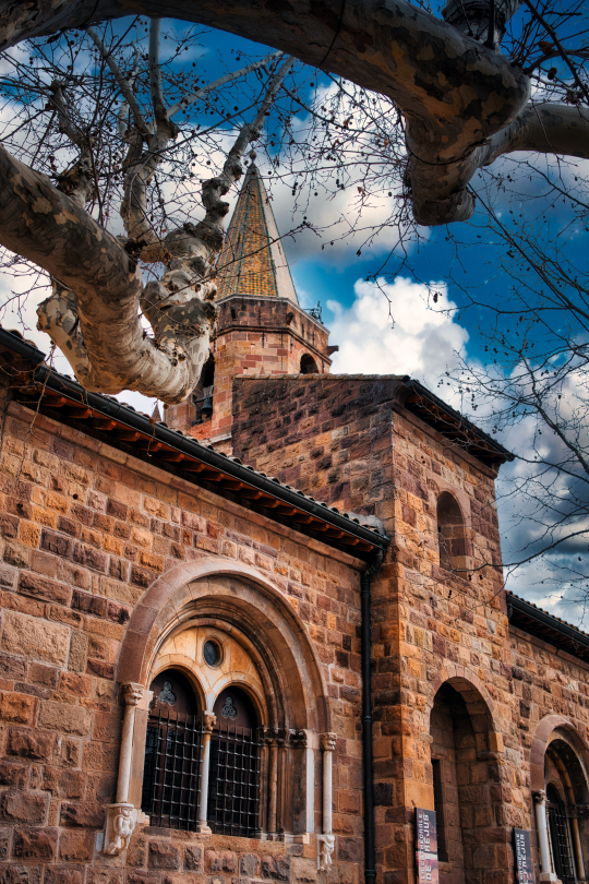 Édifice en pierre roussâtre avec une tour, sous un ciel nuageux bleu.