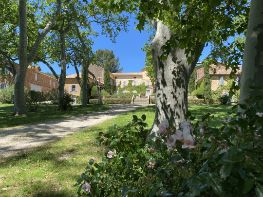 Un beau manoir entouré d'un jardin verdoyant et d'arbres, sous un ciel bleu éclatant.