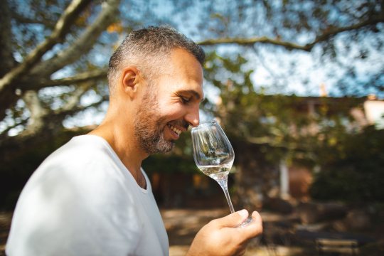 Un homme savoure un verre de vin blanc en plein air, souriant avec plaisir.