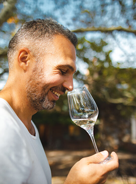 Un homme savoure un verre de vin blanc en plein air, souriant avec plaisir.