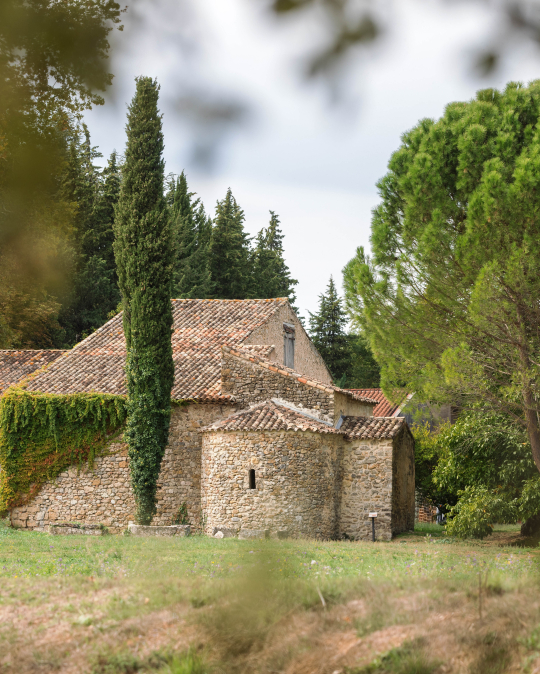 Une petite chapelle en pierre entourée de verdure et de pins, un paysage rural paisible.