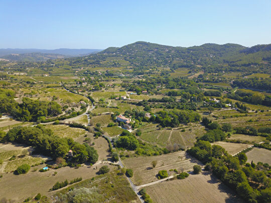 Paysage vallonné avec vignes et fermes, sous un ciel bleu clair.