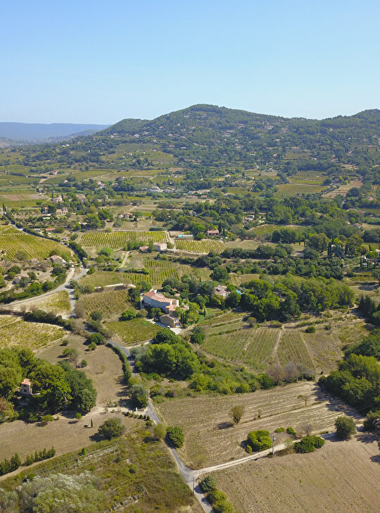 Paysage vallonné avec vignes et fermes, sous un ciel bleu clair.