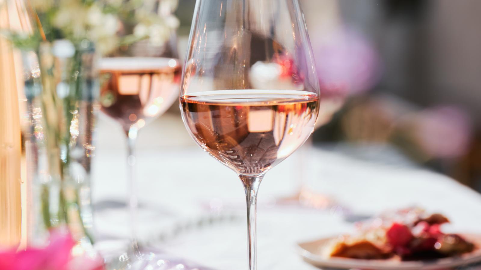 Un verre de rosé pétillant sur une table élégante, décorée de fleurs et de fruits.