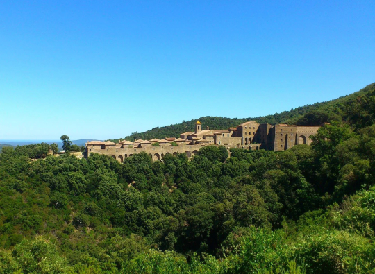 Un village médiéval perché sur une colline, sous un ciel bleu éclatant.