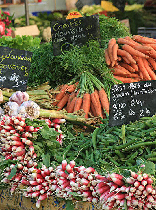 Un marché coloré avec des légumes frais : carottes, oignons, ail et radis.