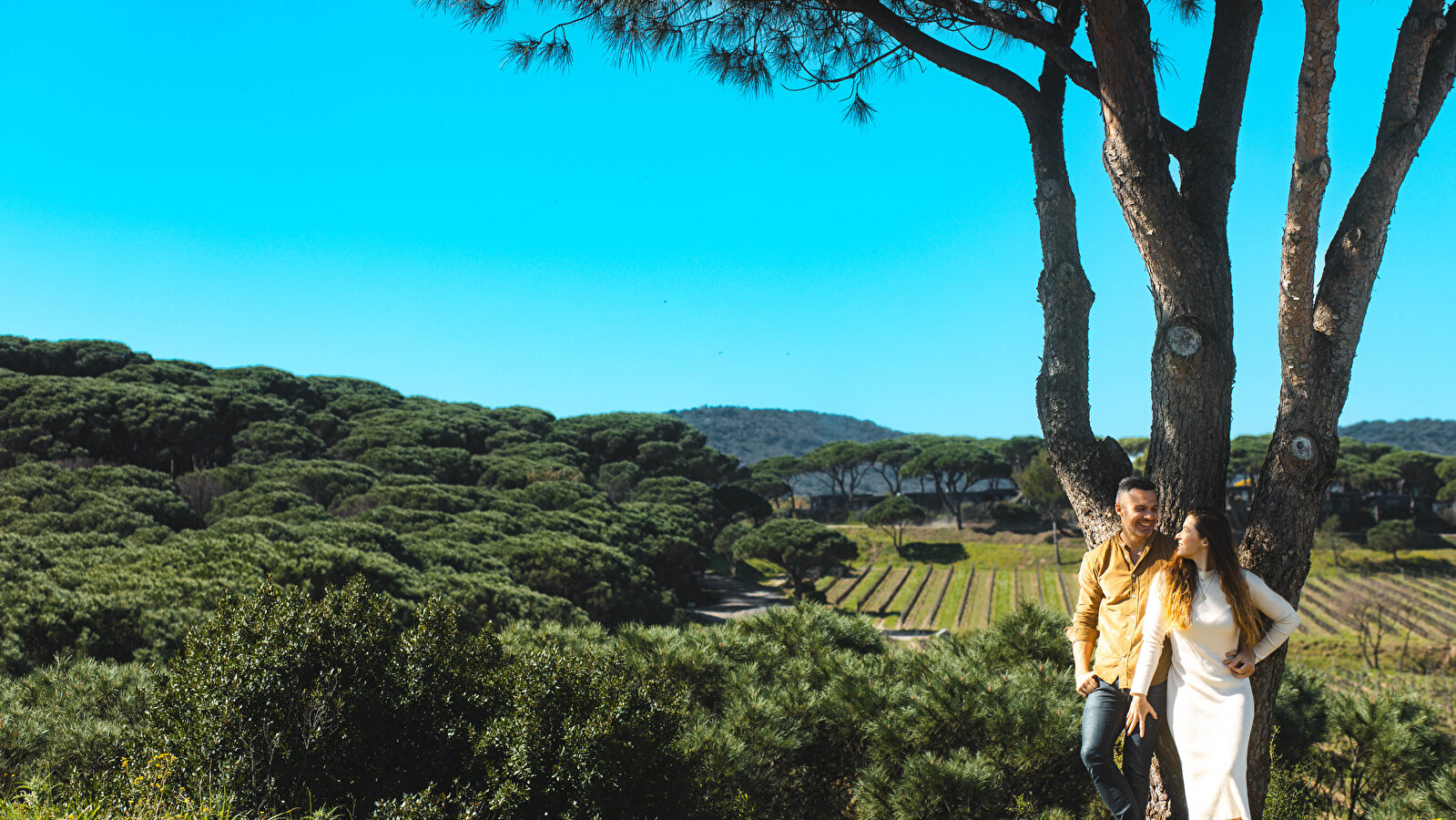 Un couple se tient près d'un arbre dans un paysage méditerranéen paisible.