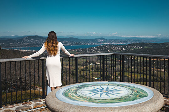 Une femme admire le paysage marin et les montagnes depuis un belvédère.