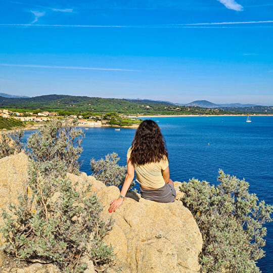 Une femme admire le paysage marin et les côtes méditerranéennes sous un ciel bleu éclatant.