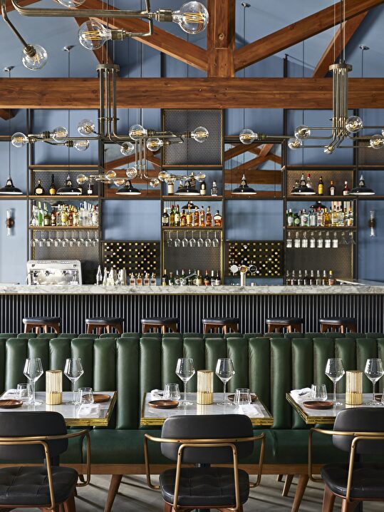 Intérieur d'un bar élégant avec des éclairages industriels et des banquettes en cuir vert.