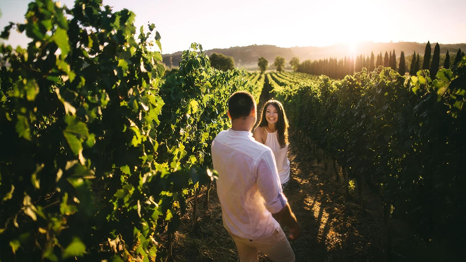 Un couple souriant se promène dans un vignoble baigné par la lumière du soleil couchant.