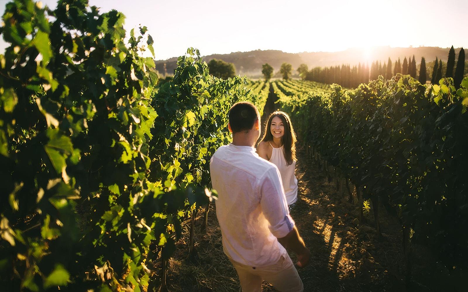 Un couple souriant se promène dans un vignoble baigné par la lumière du soleil couchant.
